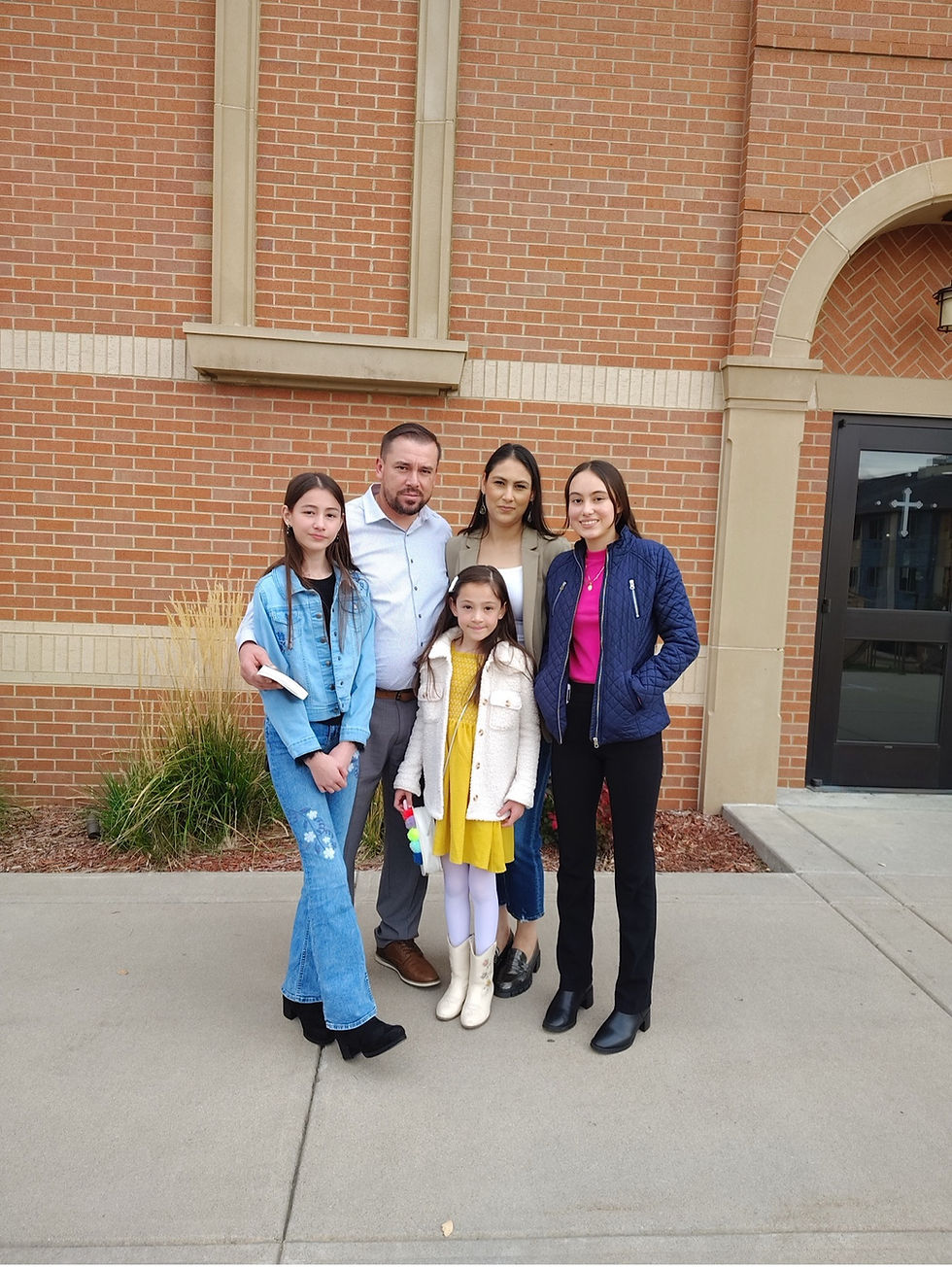 Juan and Ebelia Castañeda pose for a photo in front of Holy Trinity Parish with their three daughters